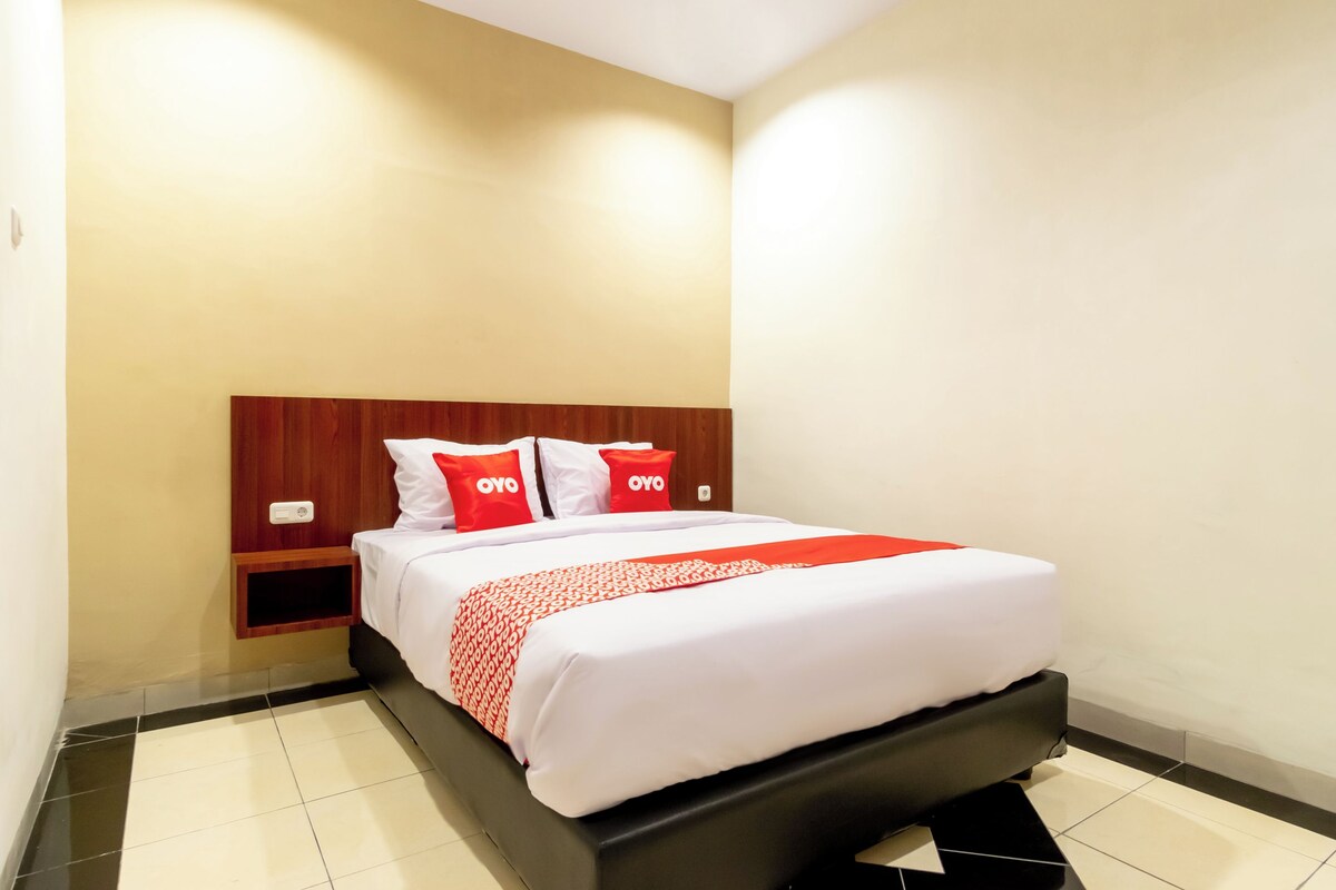 A hotel room with a bed, a wooden headboard, a bedside table, and a nightstand.