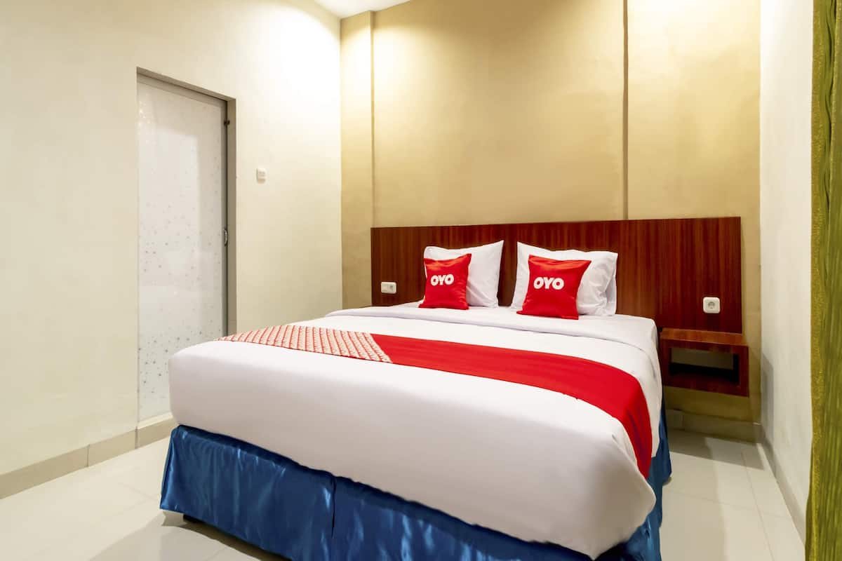 A hotel room with a large bed, a wooden headboard, and two red pillows with the logo "OYO".