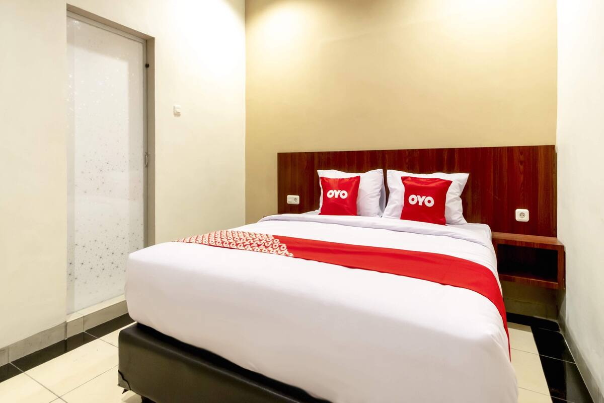A hotel room with a bed, a wooden headboard, and a nightstand.