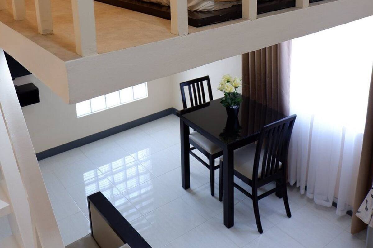 A hotel room with a bunk bed, a dining table with chairs, and a small table with a vase of flowers.