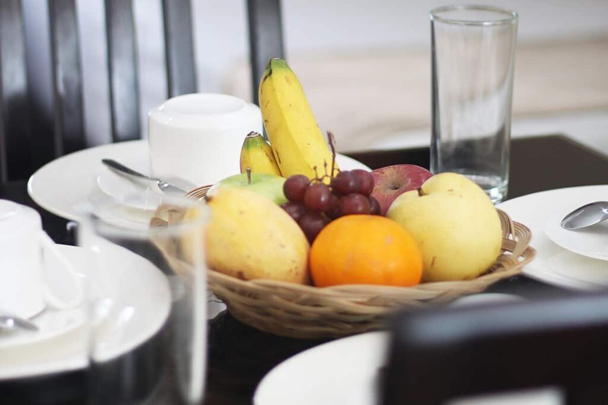 A breakfast setting with a fruit basket, a glass of water, and a white cup on a table.