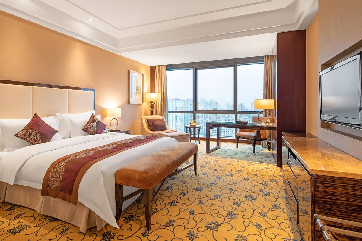 A hotel room with a large bed, a desk, and a TV.