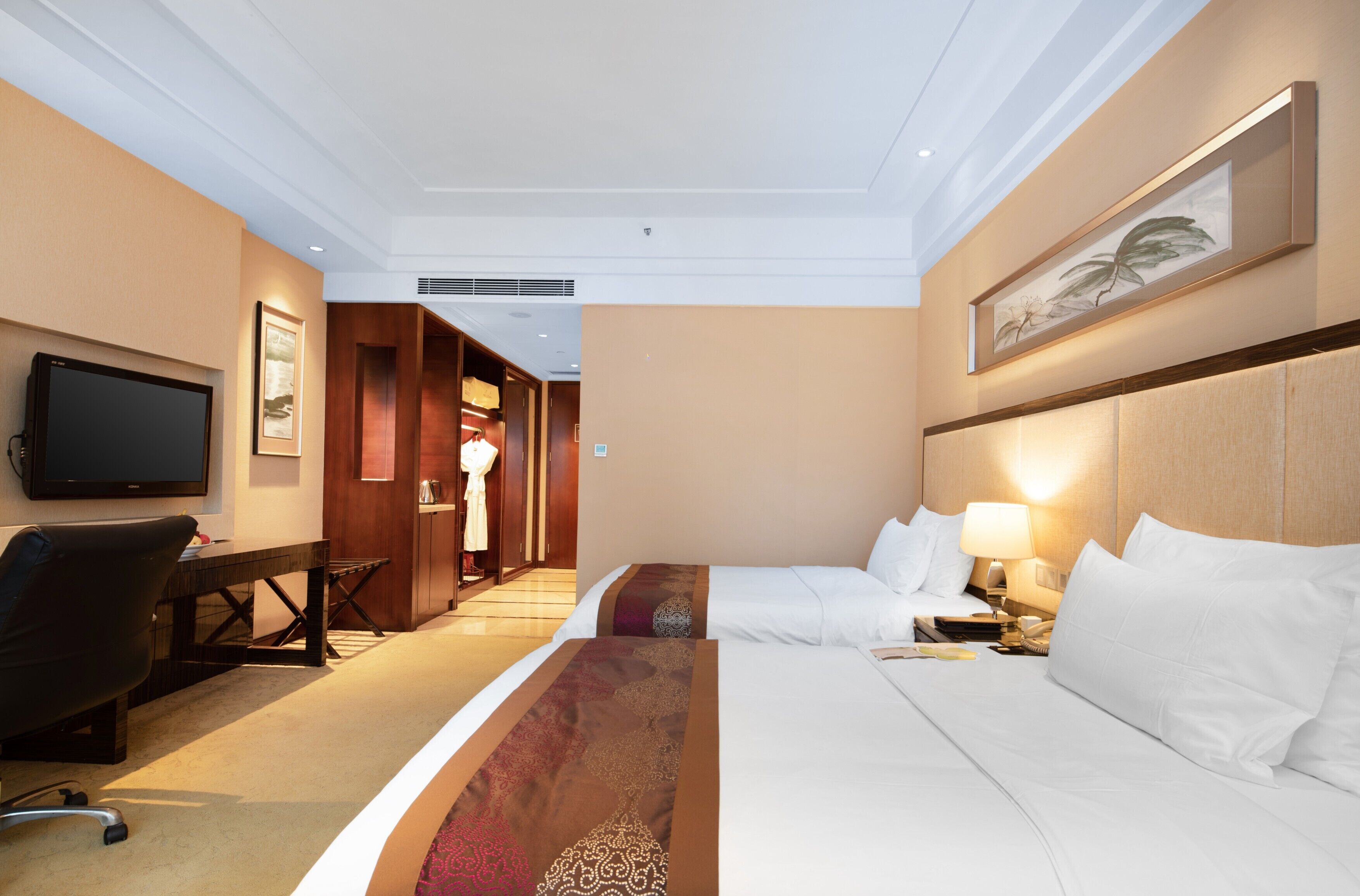 Een hotelkamer met een bed, een bureau met stoel, een televisie en een lijst aan de muur.