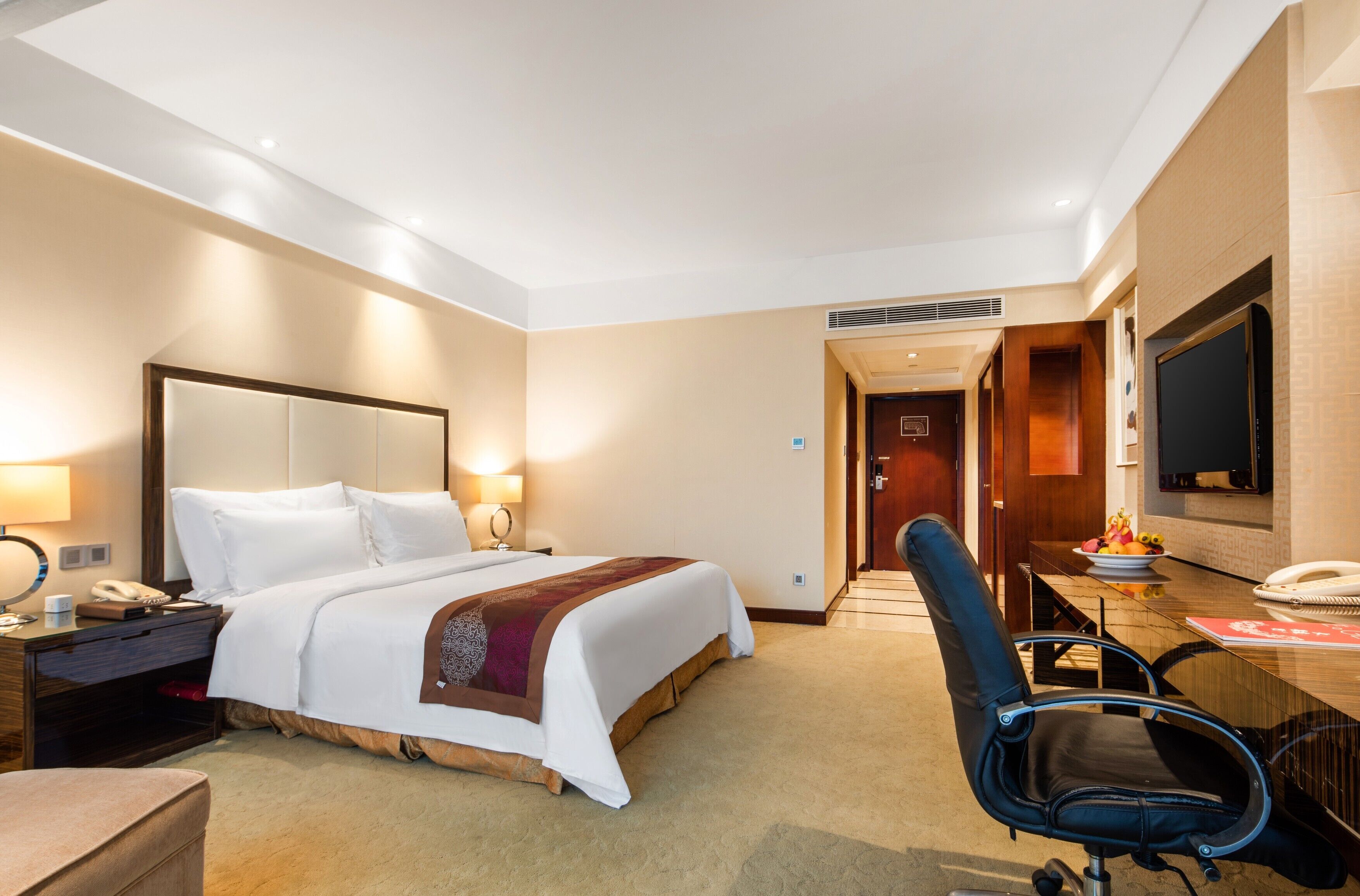 Una habitación de hotel con cama, mesita de noche, lámpara, silla, escritorio y televisor.