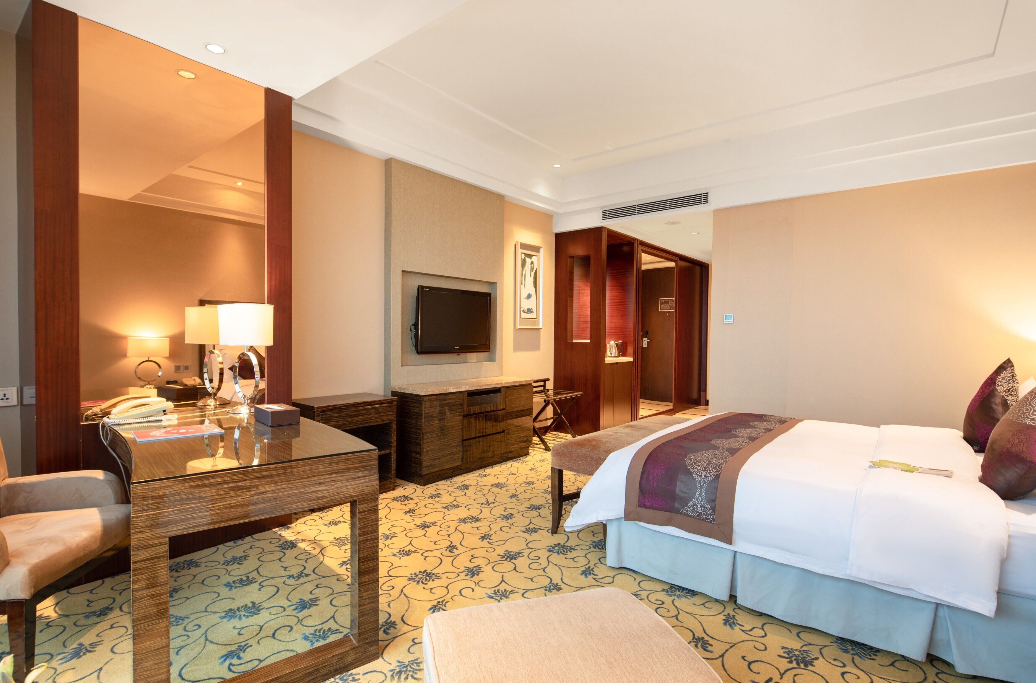 Una habitación de hotel con cama, escritorio, silla, televisor y armario.