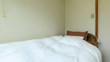 A single bed with white bedding in a room with plain walls and a wooden door frame.
