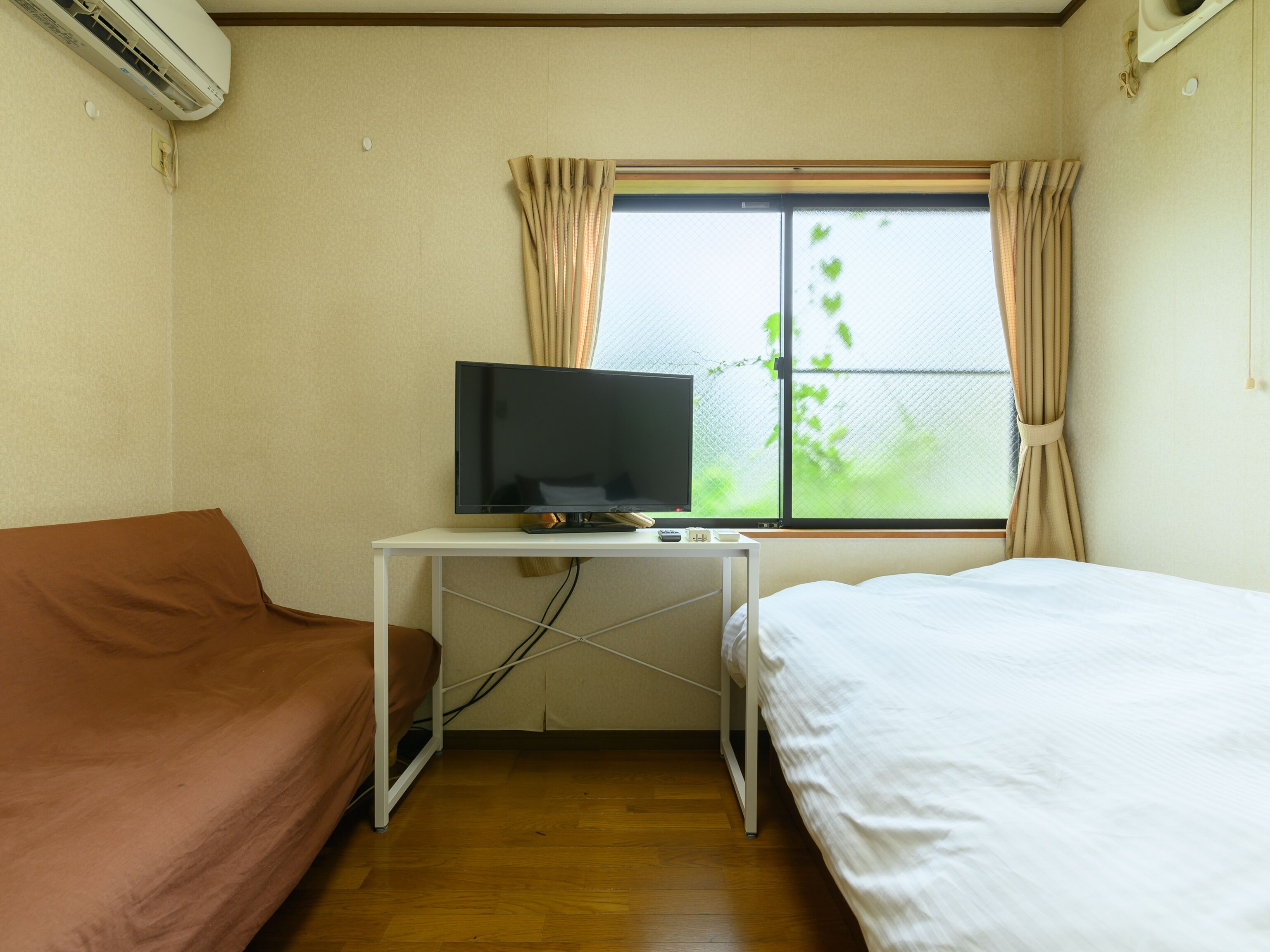 A hotel room with a bed, a sofa, a TV on a desk, and a window with curtains.