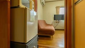 Habitación compacta con kitchenette equipada con refrigerador, microondas y estufa. Una cama está colocada contra la pared y un televisor está montado sobre una pequeña mesa.