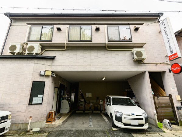 A building with a garage entrance, a white car parked inside, and a sign indicating a Tabist service. - Tabist Tatsumi Business Hotel Matsusaka (Matsusaka)