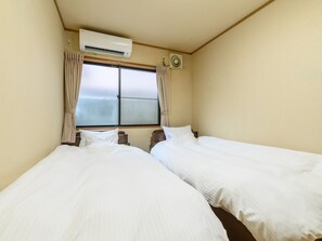 A hotel room with two beds, an air conditioning unit, a window with curtains, and a wall-mounted fan. - Tabist Tatsumi Business Hotel Matsusaka (Matsusaka)