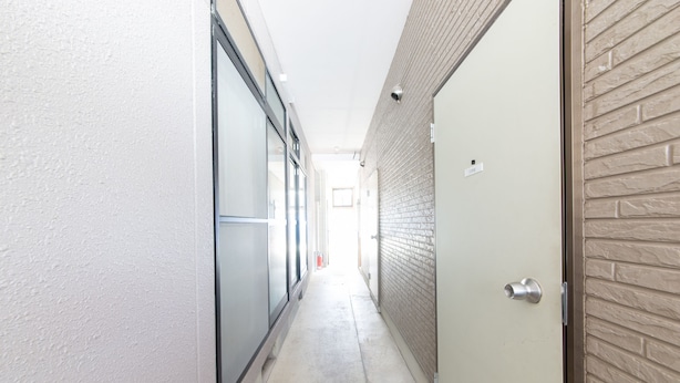 Un pasillo estrecho con suelo de concreto, una puerta con manija de metal y una pared con diseño de ladrillo.