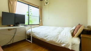 Un dormitorio con cama, televisor sobre un mueble bajo, ventana con cortinas y aire acondicionado.
