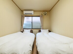 A room with two beds, an air conditioning unit, a window with curtains, and a wall-mounted fan. - Tabist Tatsumi Business Hotel Matsusaka (Matsusaka)