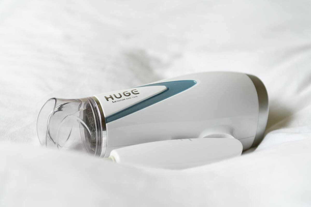 Una tetera eléctrica blanca y azul turquesa con el nombre de marca "HUGE" sobre un edredón blanco.