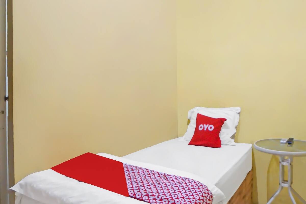 A small, single-bed room with a red and white bedspread, a red pillow with "OYO" text, and a small round table with a glass top.