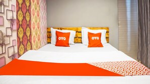 A hotel room with a bed, two pillows with 'OYO' branding, a patterned wall, and a window with curtains. - OYO 990 Stadion Residence Syariah (Medan)