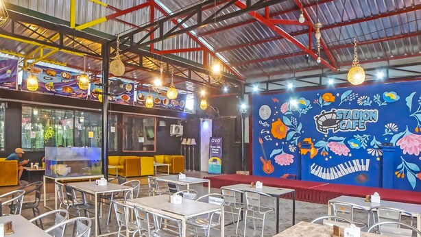A spacious cafe with high ceilings, metal chairs, and tables. - OYO 990 Stadion Residence Syariah (Medan)