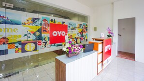 A reception area with a glass wall displaying colorful artwork, a reception desk with a laptop, and a vase of flowers. - Super OYO 1838 COZY Home (Manado)