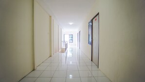 A long, narrow hallway with white tiled floors and walls, leading to a door at the end. - Super OYO 1838 COZY Home (Manado)