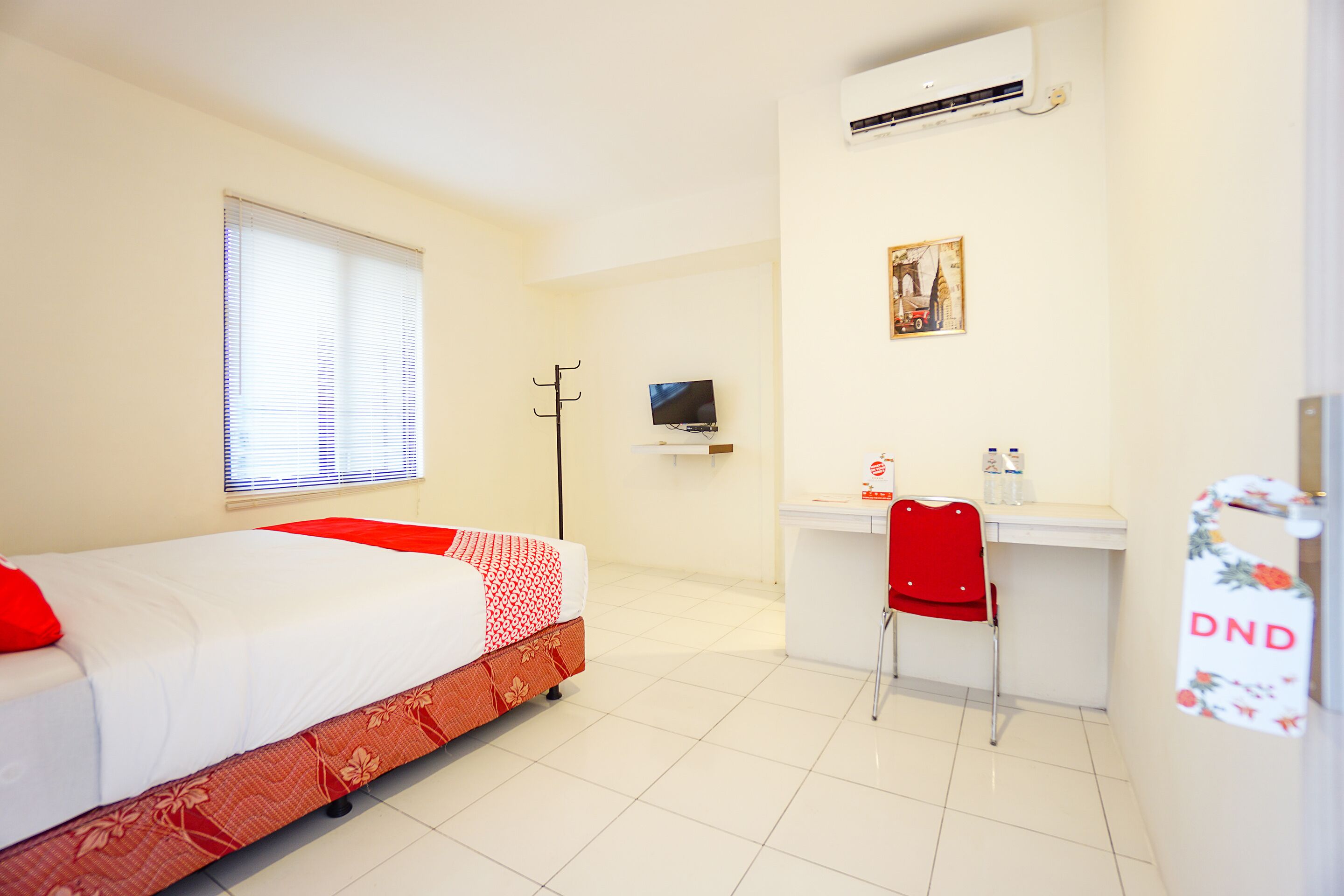 A hotel room with a bed, a desk, a chair, a television, and an air conditioning unit.