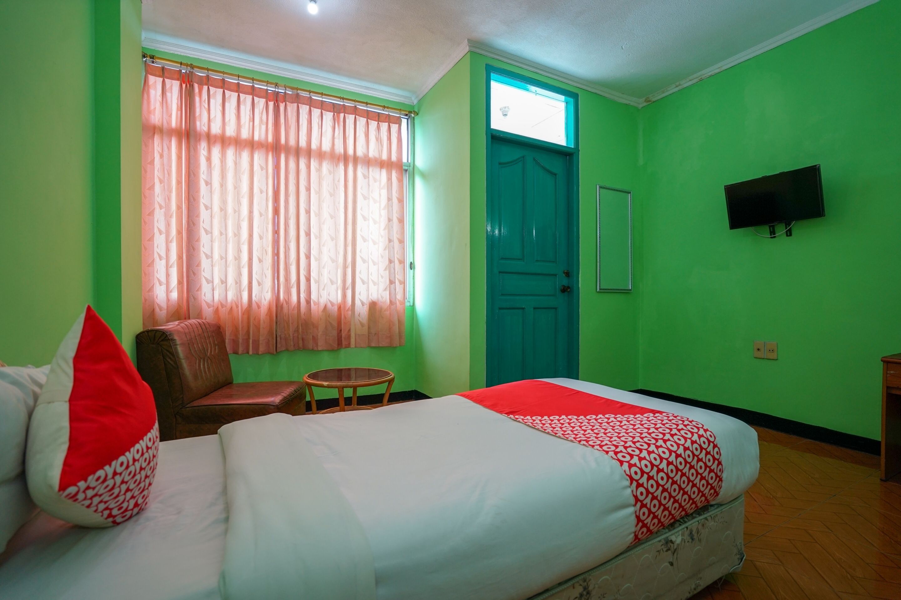 A room with a bed, a chair, a small table, a TV mounted on the wall, and a door.
