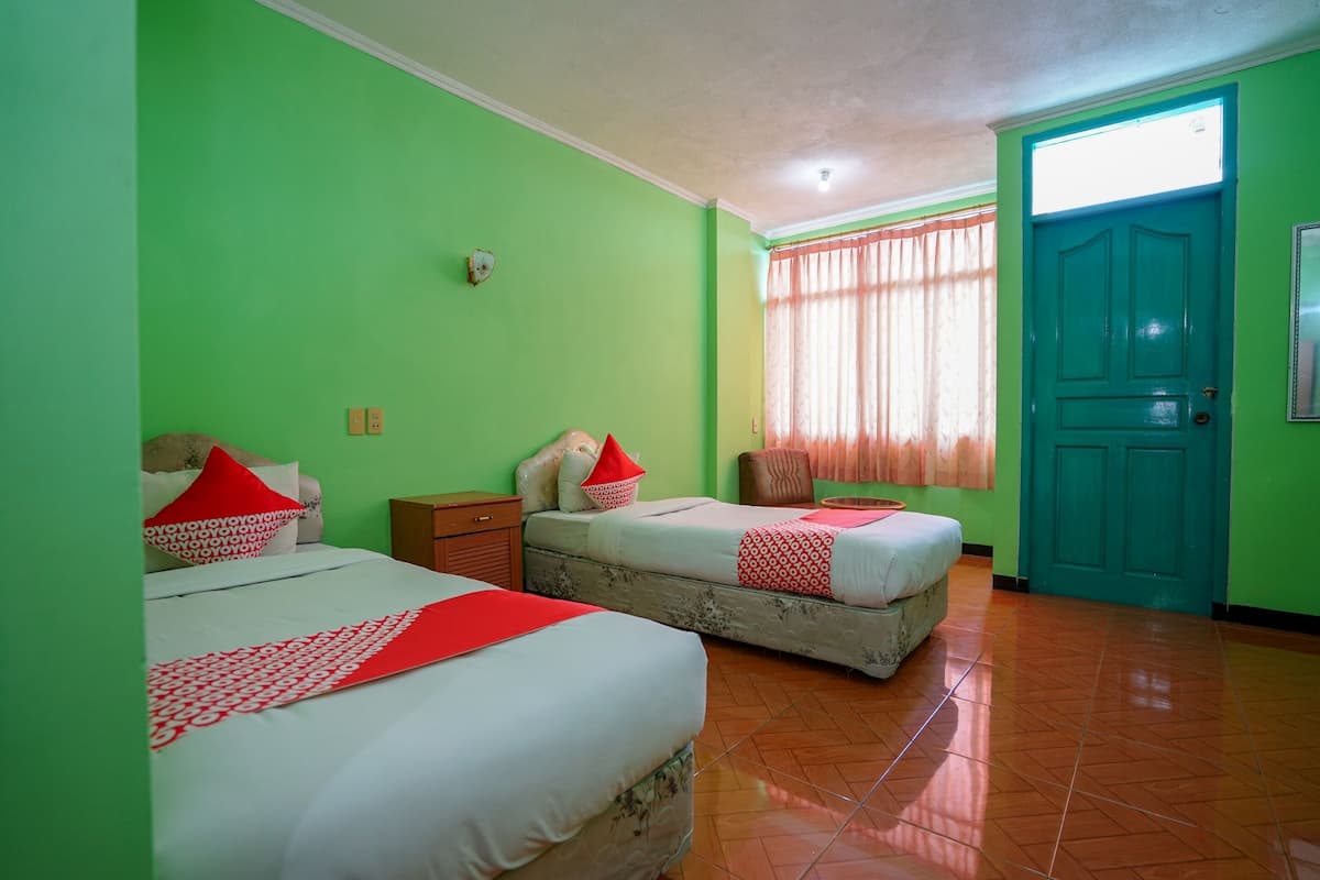 Une chambre avec deux lits, une porte de couleur turquoise et une fenêtre avec des rideaux.
