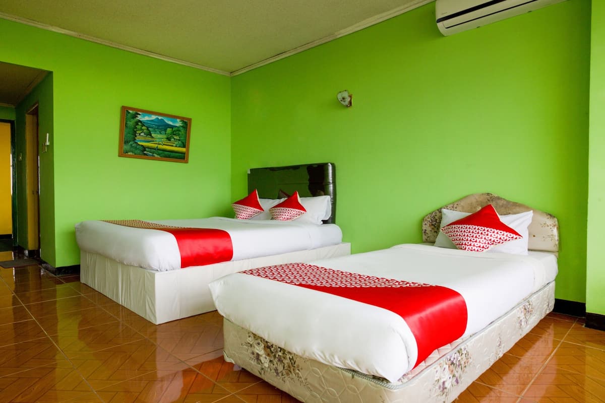 Une chambre d’hôtel avec deux lits, des murs verts et un tableau accroché au mur.