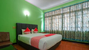 Ein Zimmer mit einem Bett, grünen Wänden, einem braunen Ledersessel und einem Fenster mit gemusterten Vorhängen.