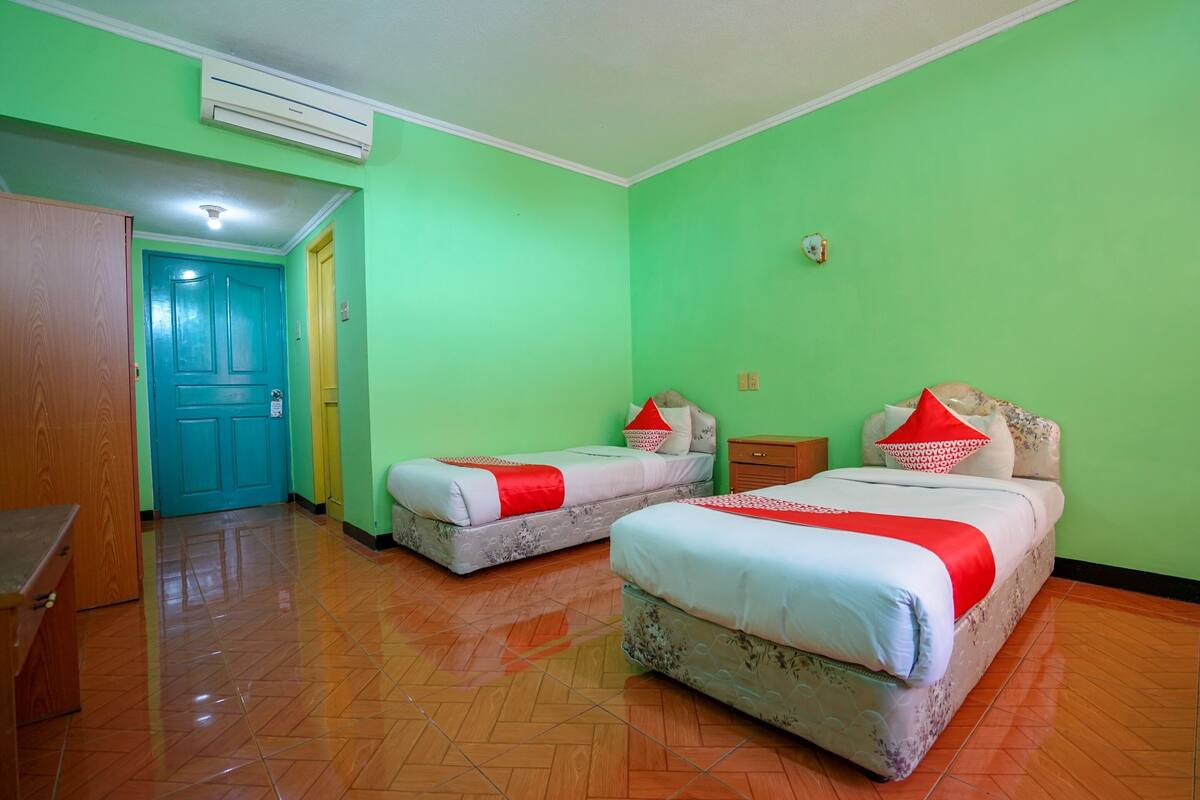Une chambre avec deux lits, des murs verts et un plancher en bois.