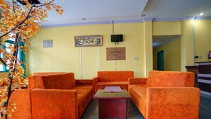 Eine Lobby mit orangefarbenen Sofas, einem kleinen Tisch, einem gerahmten Kunstwerk, einer Plakette und einem Fernseher.