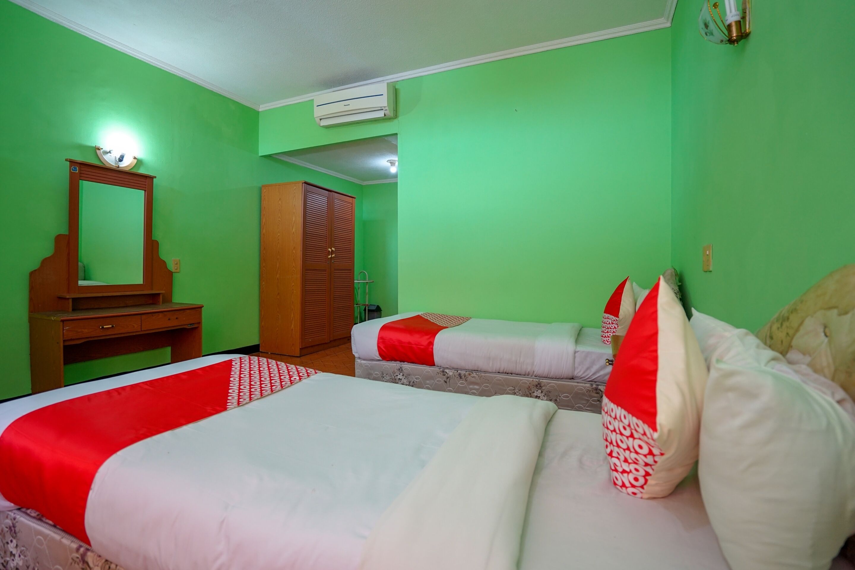Een kamer met twee bedden, een houten garderobe, een spiegel en een airconditioning.