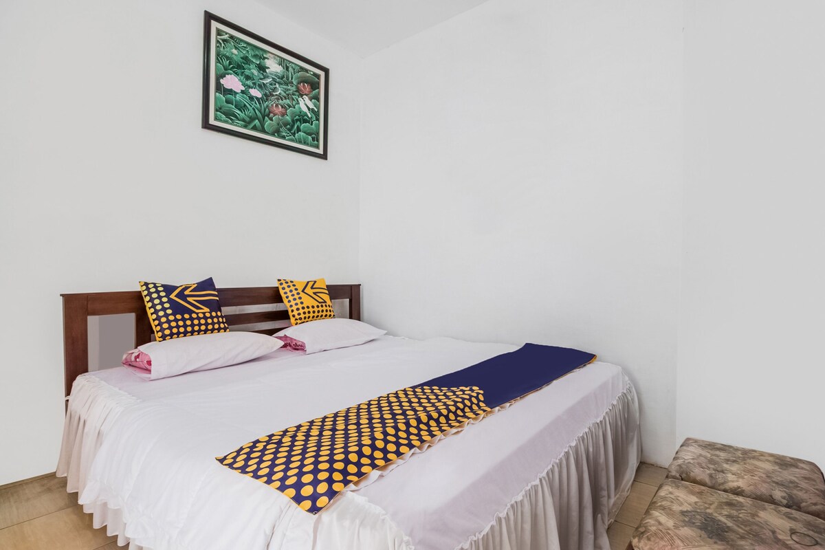 A neatly made bed with a white and blue bedspread, two pillows with yellow patterns, and a blue blanket.