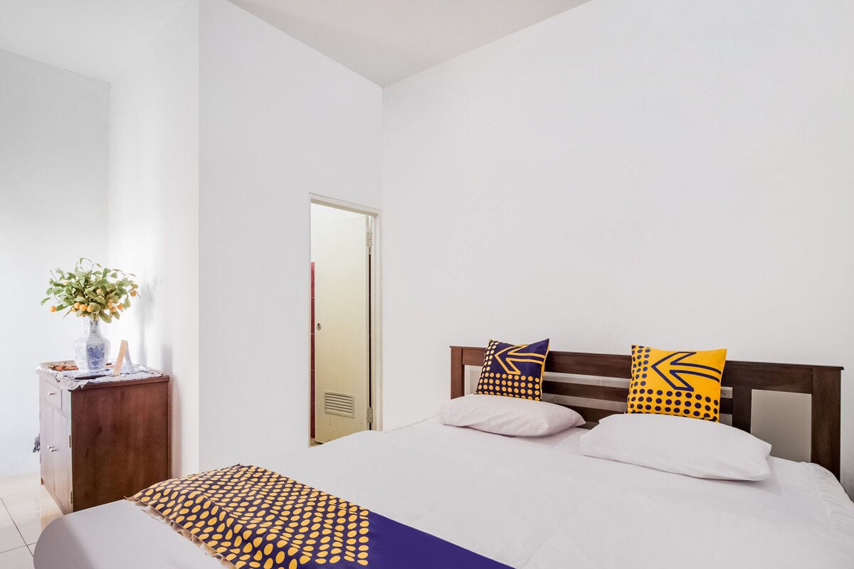 A bedroom with a bed, a wooden headboard, a bedside table with a vase, and a door.