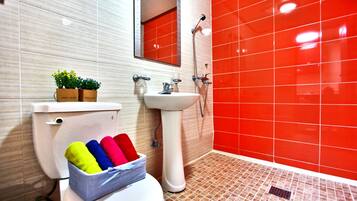 A bathroom with a toilet, sink, and shower. There is a basket of colorful bath towels on the toilet.