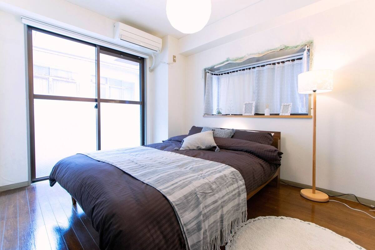 Un dormitorio con una cama grande, una mesita de noche, una lámpara y una ventana con cortinas.