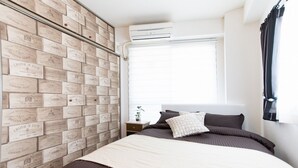 A bedroom with a bed, pillows, a nightstand, a window with curtains, and a wall with vintage-style plaques.