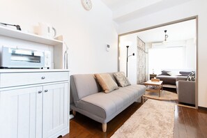 A modern living room with a grey sofa, a small coffee table, and a white cabinet with a microwave. - Omotenashi House Kawaguchi (Kawaguchi)