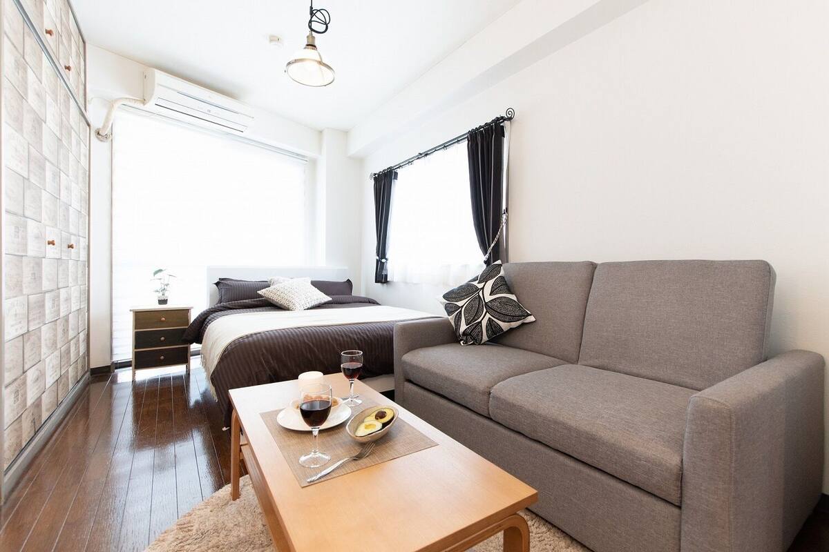 Un dormitorio moderno con cama, un sofá gris, una mesa de madera con alimentos para el desayuno y una ventana con cortinas.
