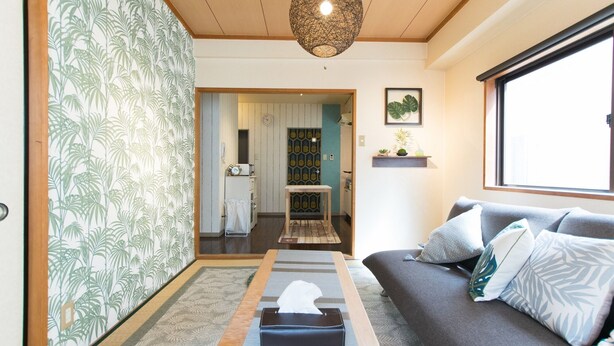 A living room with a sofa, a table with a tissue box, a patterned rug, a hanging light fixture, and a window with a view.