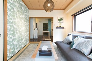 Una sala de estar con un sofá, una mesa con una caja de pañuelos, una alfombra estampada, un candelabro colgante y una ventana con vistas.