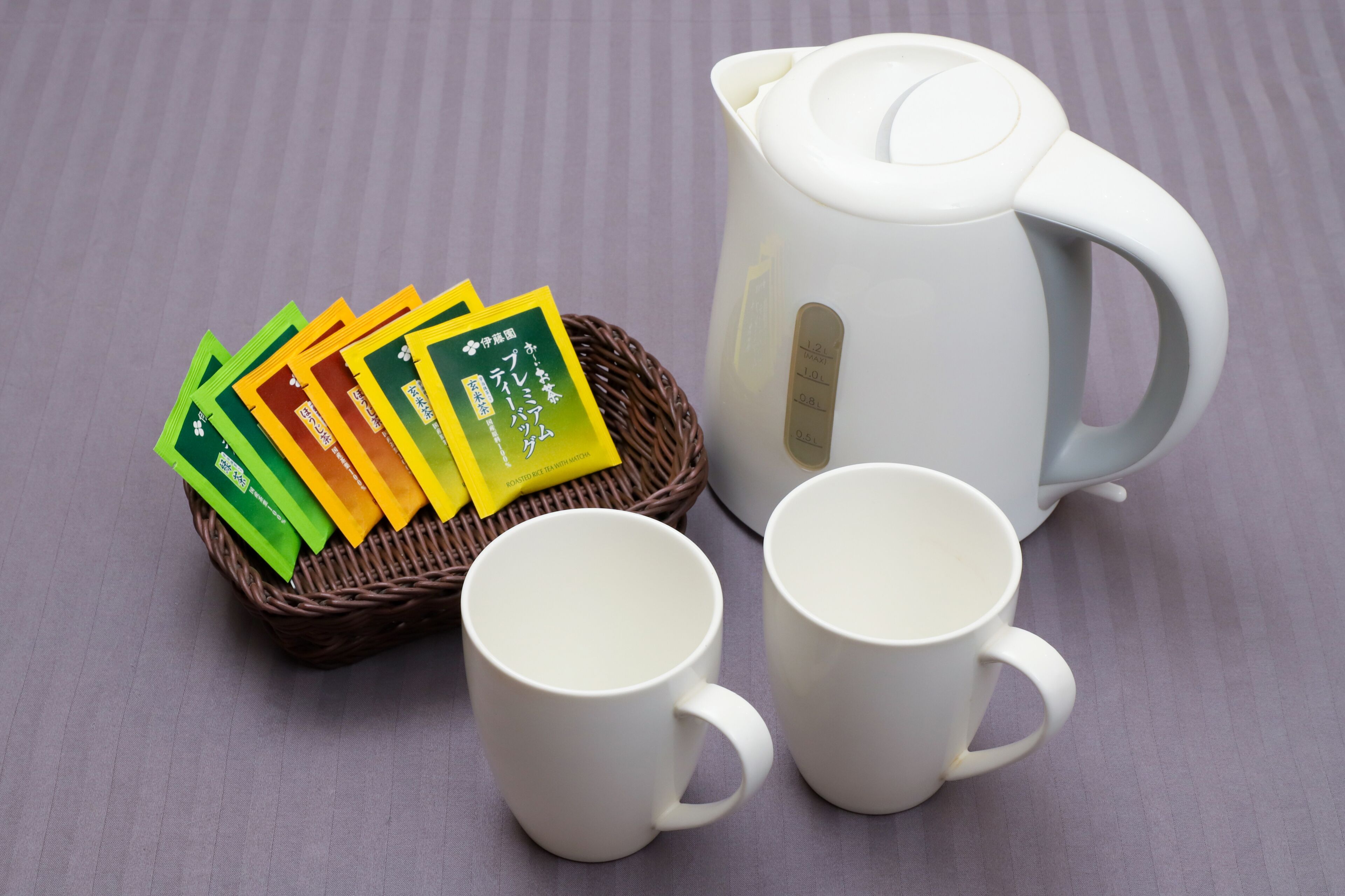 Una tetera blanca, dos tazas blancas y una cesta de mimbre con bolsitas de té.