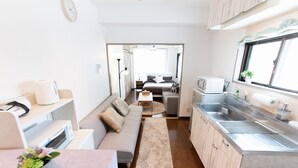 A compact kitchenette with a microwave, sink, and countertop. A sofa and a small table with a vase of flowers are in the living area.