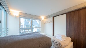 Ein Schlafzimmer mit einem großen Bett, einem Holzschrank, einem Fenster mit Blick auf Gebäude und einem Balkon.