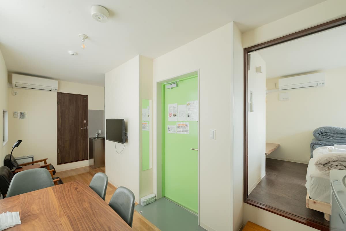 Habitación de hotel con una mesa de comedor de madera, una puerta verde, una cama con estructura de madera y un escritorio pequeño con una silla.