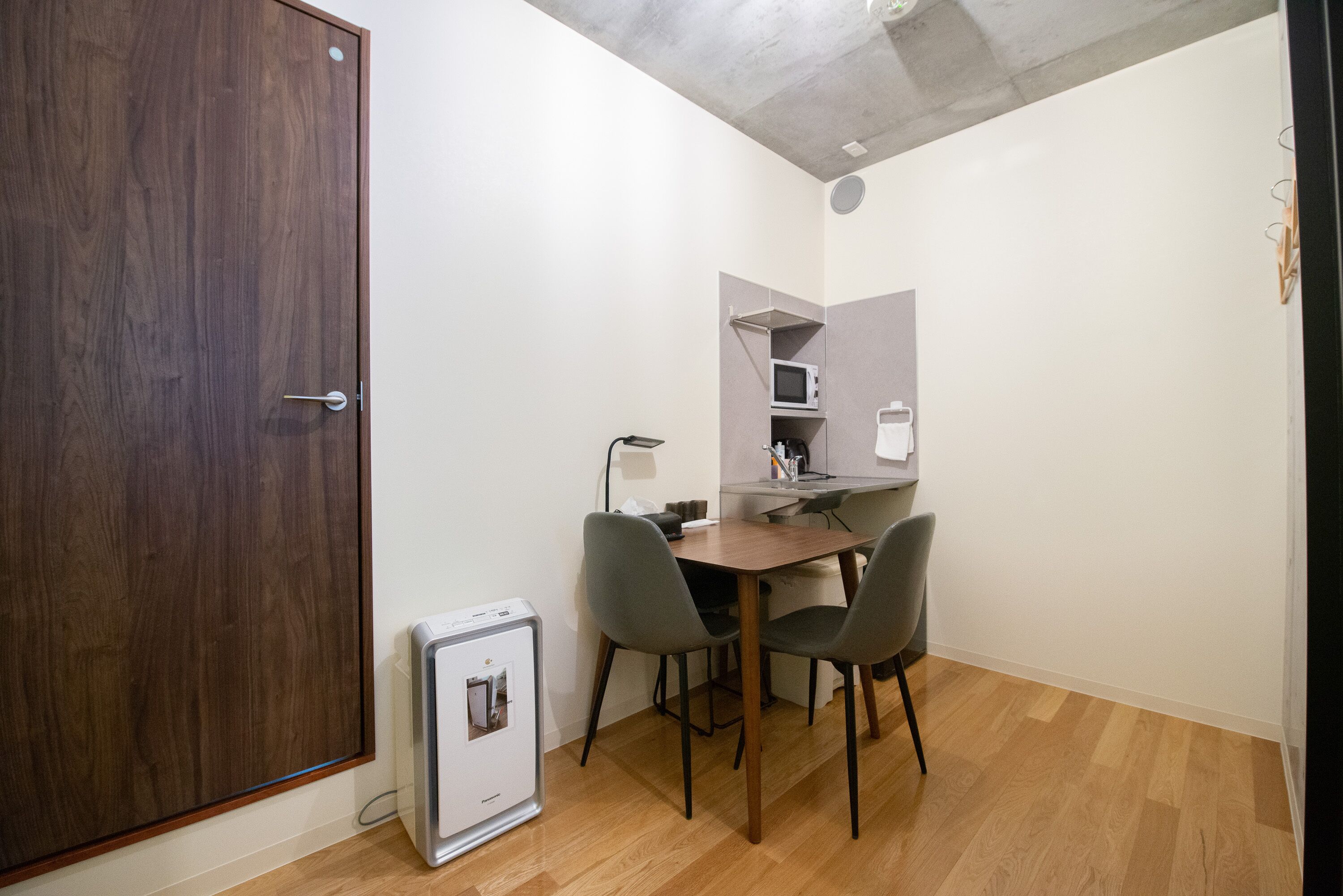 Une pièce de taille modeste avec une porte en bois, une petite kitchenette équipée d’un four à micro-ondes, une table avec deux chaises et un réfrigérateur compact.
