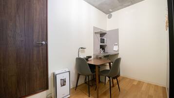Une pièce de taille modeste avec une porte en bois, une petite kitchenette équipée d’un four à micro-ondes, une table avec deux chaises et un réfrigérateur compact.
