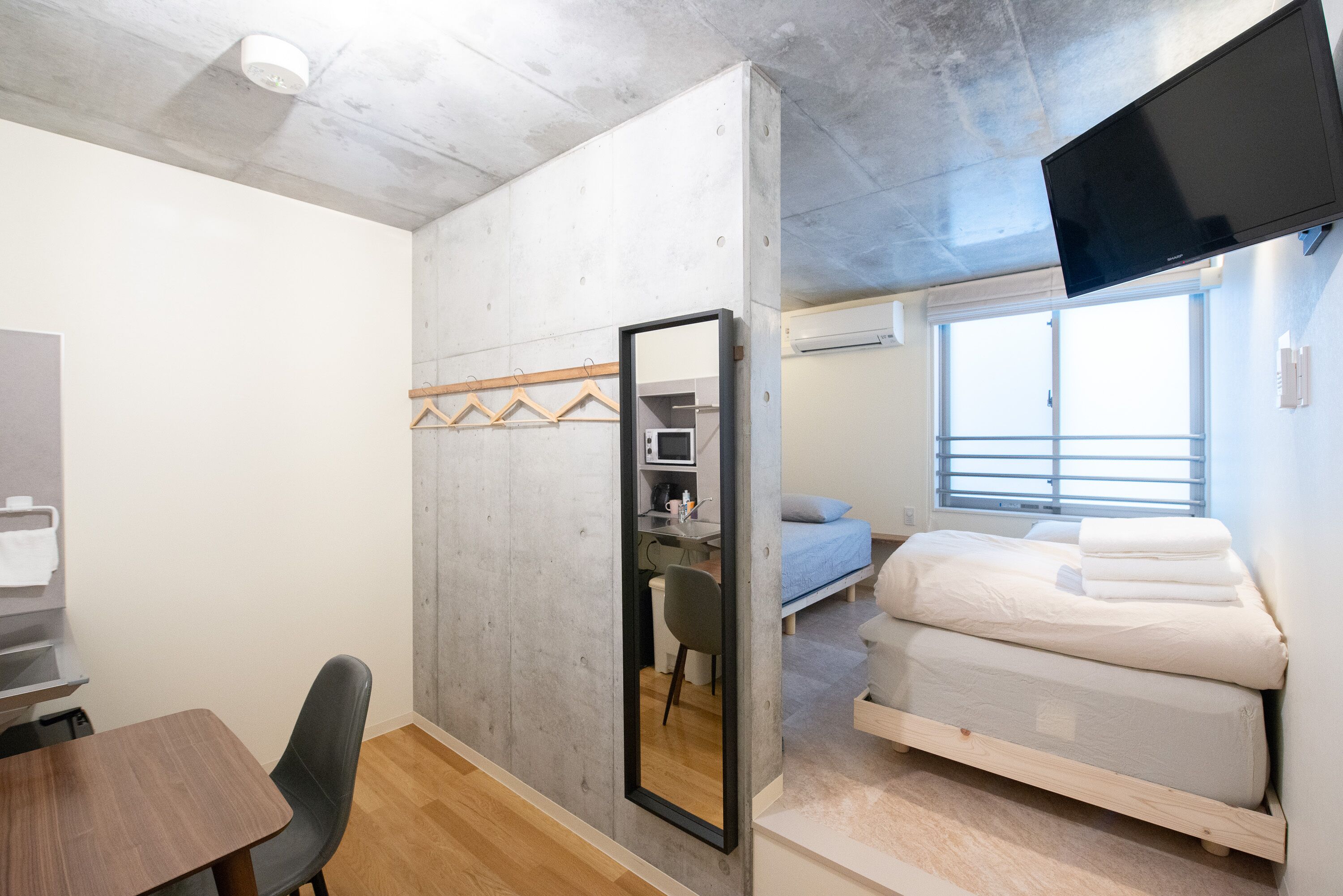 A compact room with a bed, a desk, a chair, a mirror, and a TV mounted on the wall.