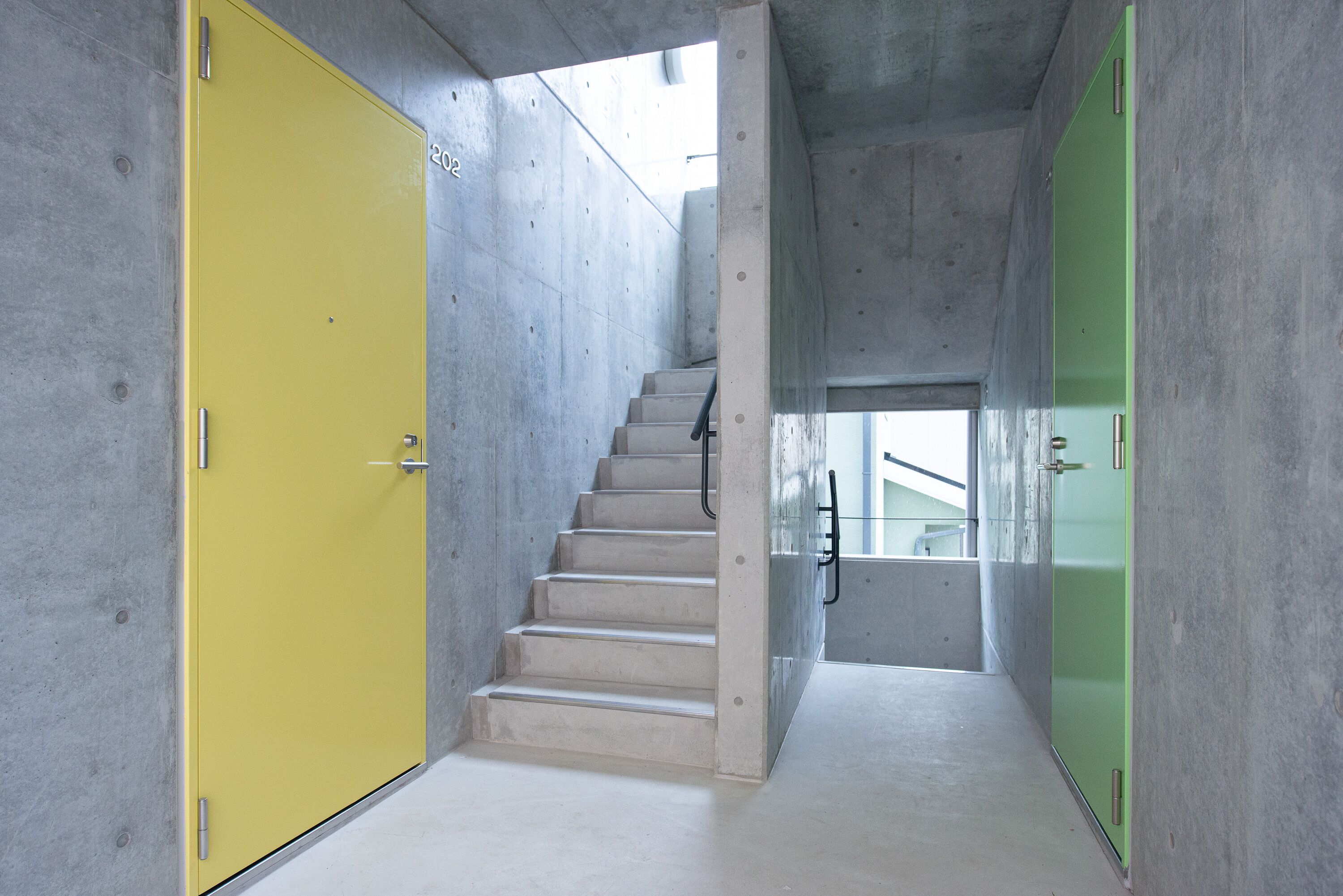 A staircase with a yellow door on the left and a green door on the right, leading to a lower level.
