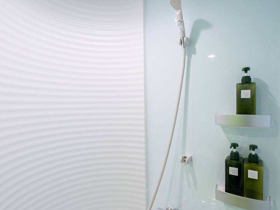 A modern bathroom with a curved ceiling, a shower with a handheld showerhead, and two green bottles on a shelf.
