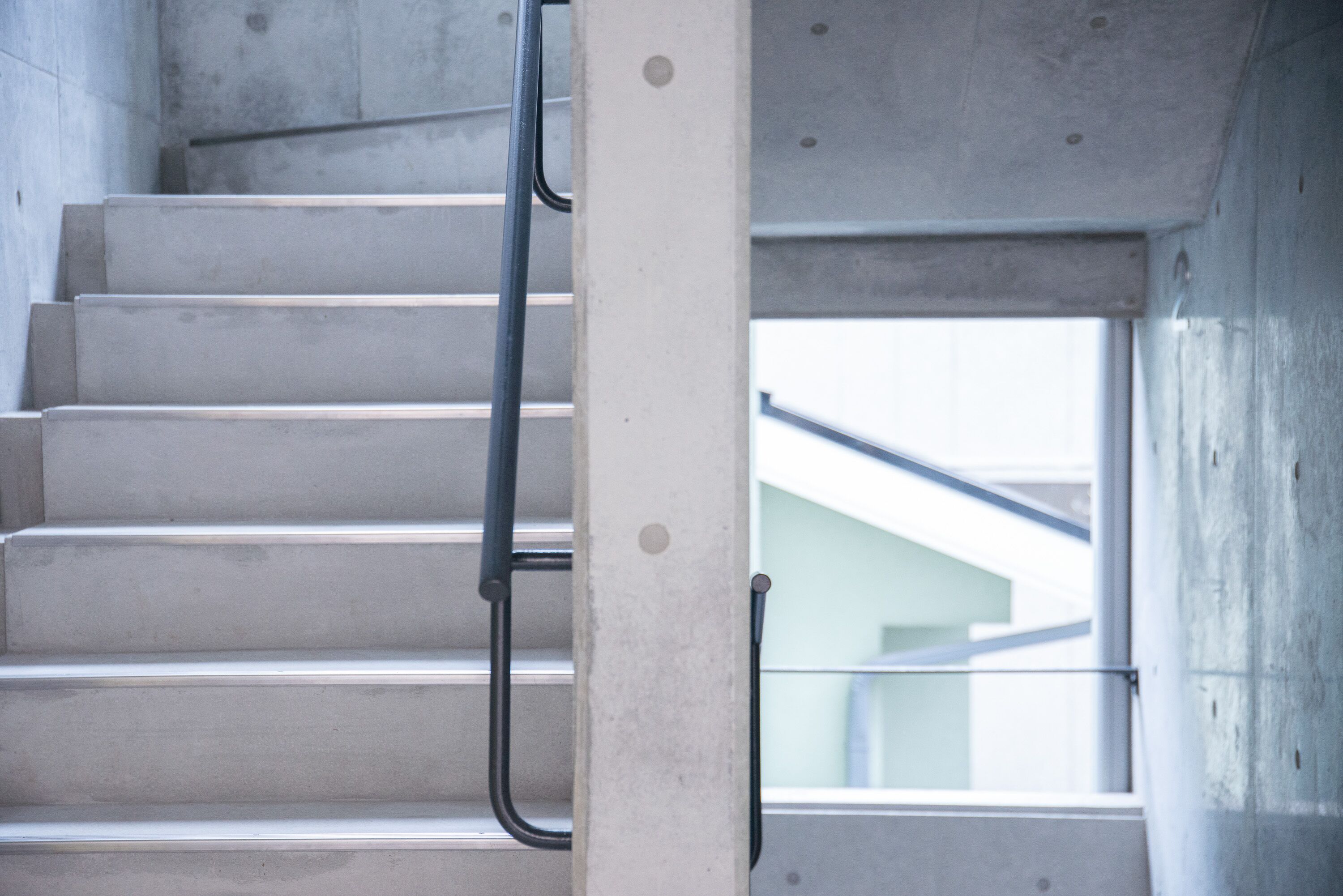 Un escalier en béton avec des rampes métalliques, menant à un balcon en verre.